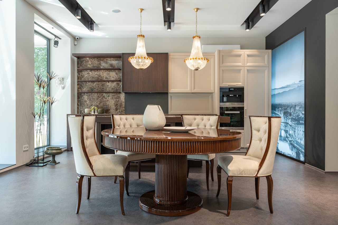 Interior of elegant spacious kitchen with wooden furniture and shiny crystal chandelier hanging over dining zone with round table and comfortable chairs